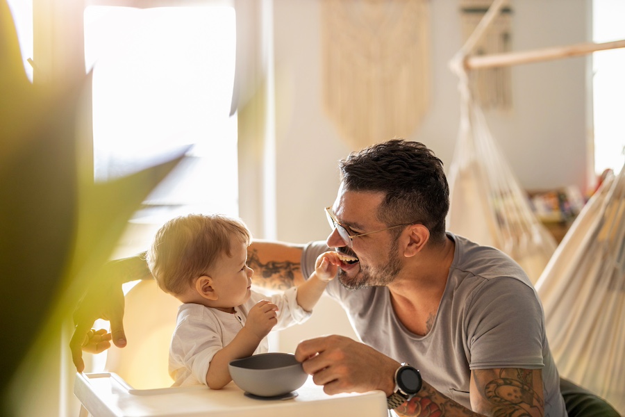 Single father sharing a joyful breakfast with his toddler in a sunny kitchen.