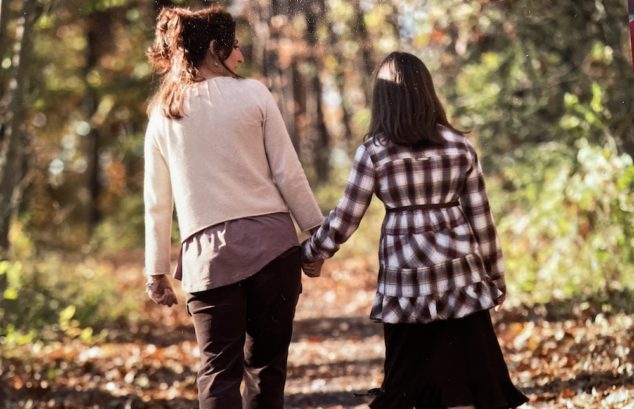 Mother and daughter holding hands while walking on a forest path.