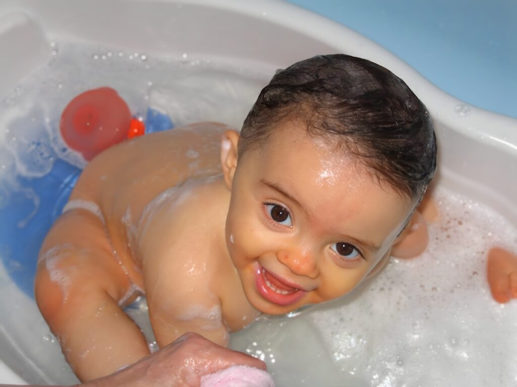 Baby smiling brightly while sitting in a small bathtub with bubbles