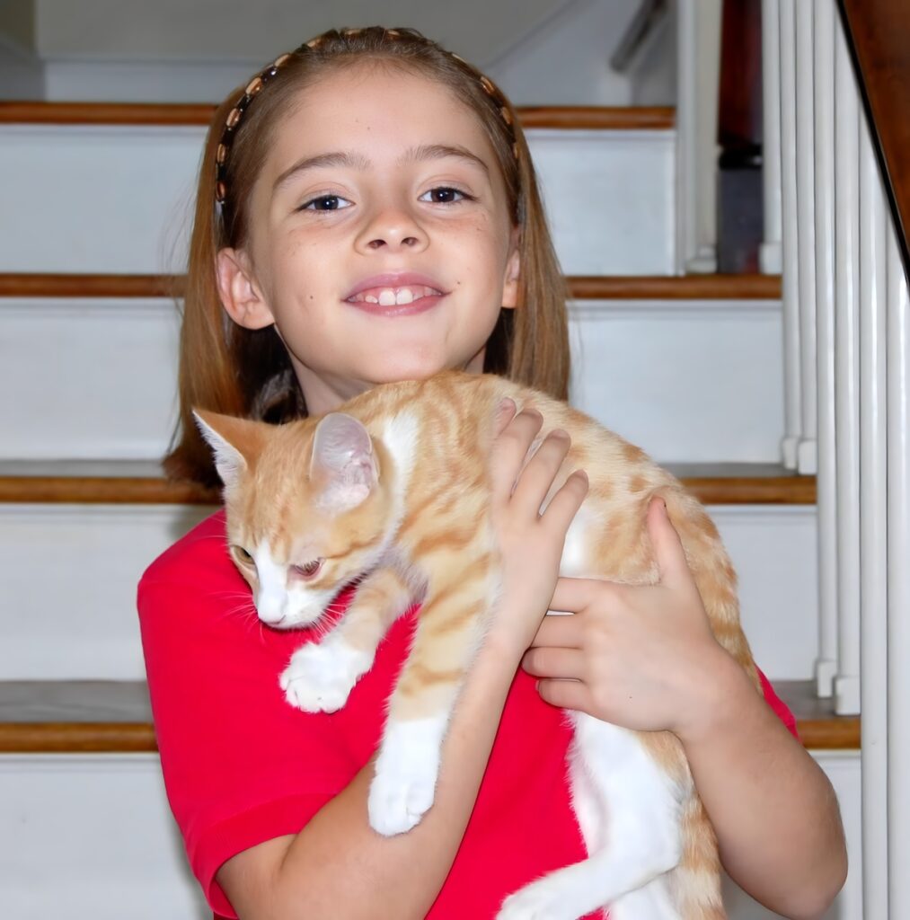 Young girl smiling while holding orange and white kitten on staircase.