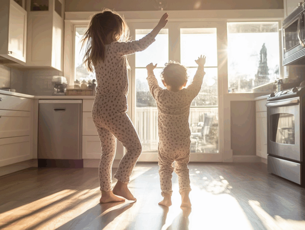 Two young kids dancing barefoot in pajamas in a sunny kitchen