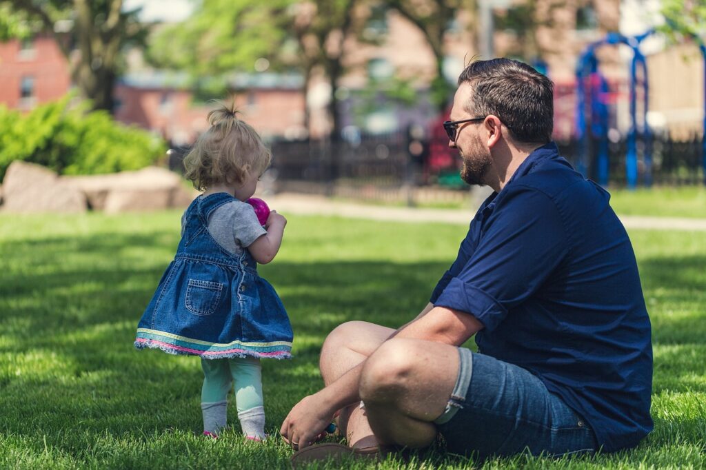 Single dad sitting in the park fully present and attentive while his toddler plays representing the heart of child-focused co-parenting
