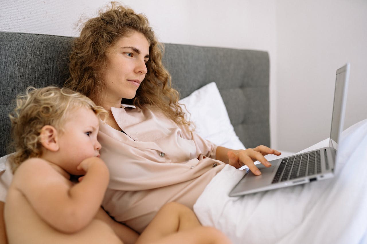 Single mom managing co-parenting communication on her laptop while caring for her young child at home